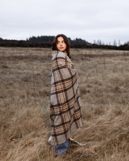 Woman wrapped in a tartan wool blanket standing in a field