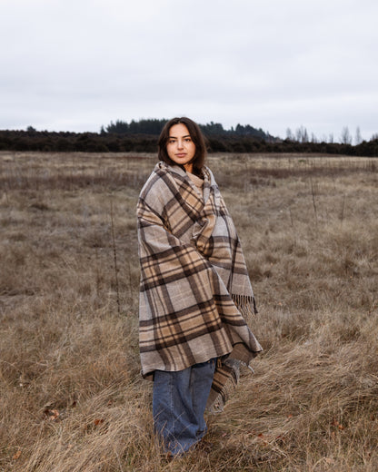 Woman wrapped in a tartan blanket standing in a field