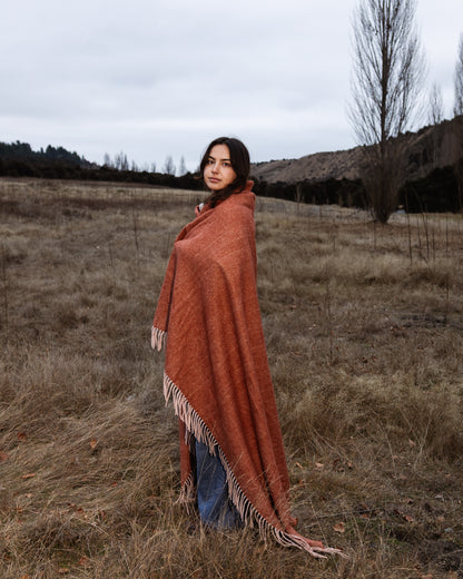 Woman wrapped in a rust-colored recycled wool blanket standing in a field.