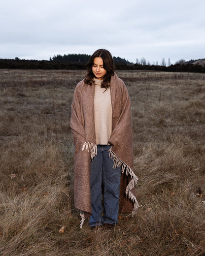 Woman wrapped in a brown recycled wool blanket standing in a field