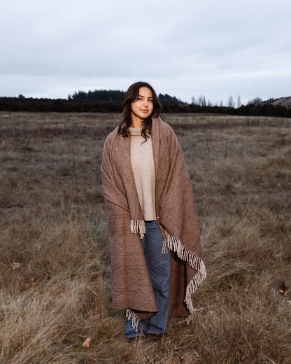 Woman wrapped in a brown recycled wool blanket standing in a field
