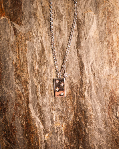 A silver necklace with a Southern Cross pendant and a separate star pendant, displayed on a wooden surface.