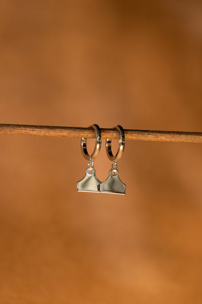 Silver hoop earrings with cattle tag pendants on a rusted fence wire