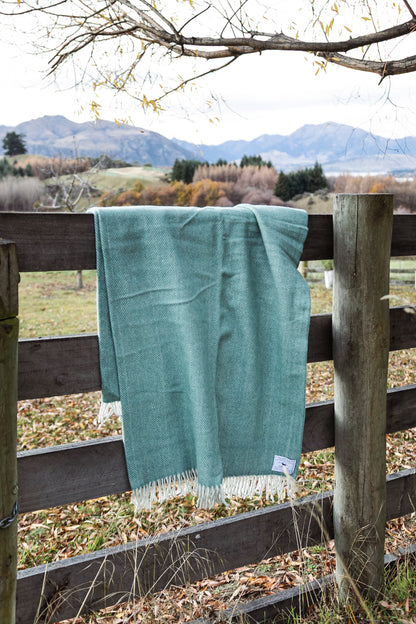 Teal blanket hanging on a wooden fence with a scenic background of mountains and fields.