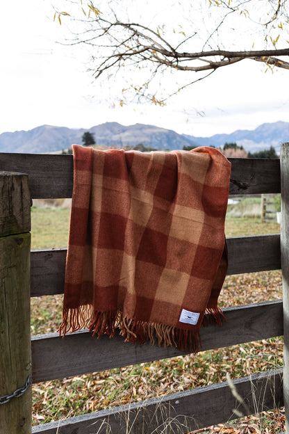 Recycled wool blanket draped over a wooden fence with a country background