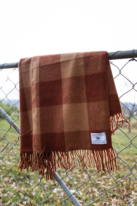 Recycled wool blanket hanging on a chain-link fence.