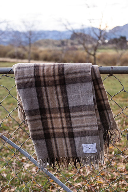 Recycled wool tartan blanket draped over a fence with a scenic background